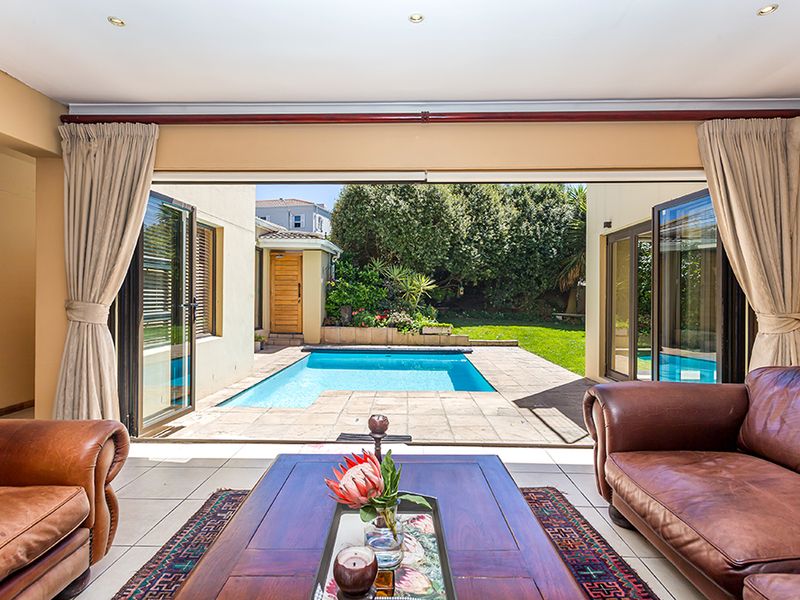 Spacious living area featuring large bi-fold doors that open onto a paved patio and swimming pool, creating a seamless indoor-outdoor flow.