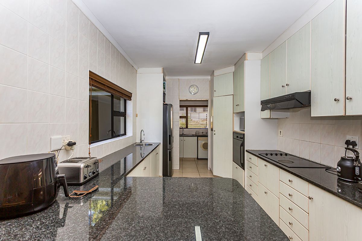 A functional kitchen featuring granite countertops, built-in cabinetry, an integrated oven, and a hob, with an adjoining scullery area visible in the background.