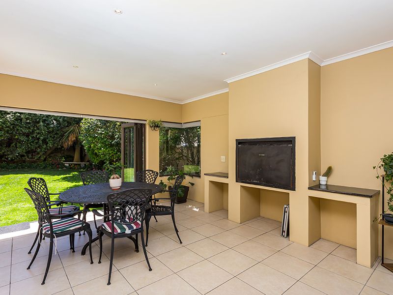 Covered patio featuring a built-in braai, granite prep surface, tiled flooring, and large stacking doors opening onto a private garden.