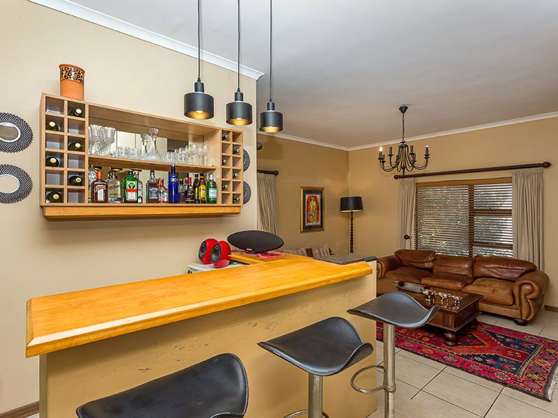 A dedicated home bar area featuring a built-in wooden counter, wall-mounted shelving, and pendant lighting, integrated into the living space.