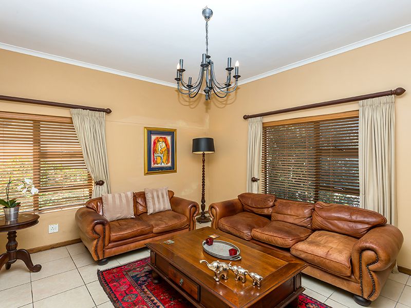 A comfortable living room featuring tiled flooring, a central chandelier, and dual windows with wooden blinds and curtain rods.