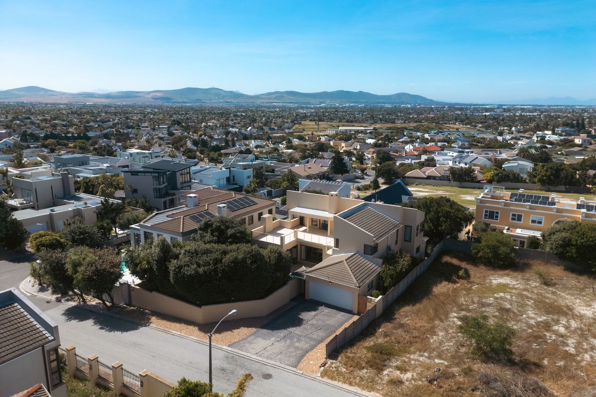Aerial view of a residential property featuring a tiled roof, solar panels, double garage, and a paved driveway within a suburban neighborhood setting.