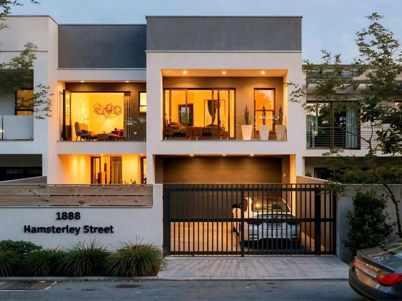 Modern two-story residential facade featuring a balcony with glass balustrades, recessed lighting, and a secure gated driveway entrance.