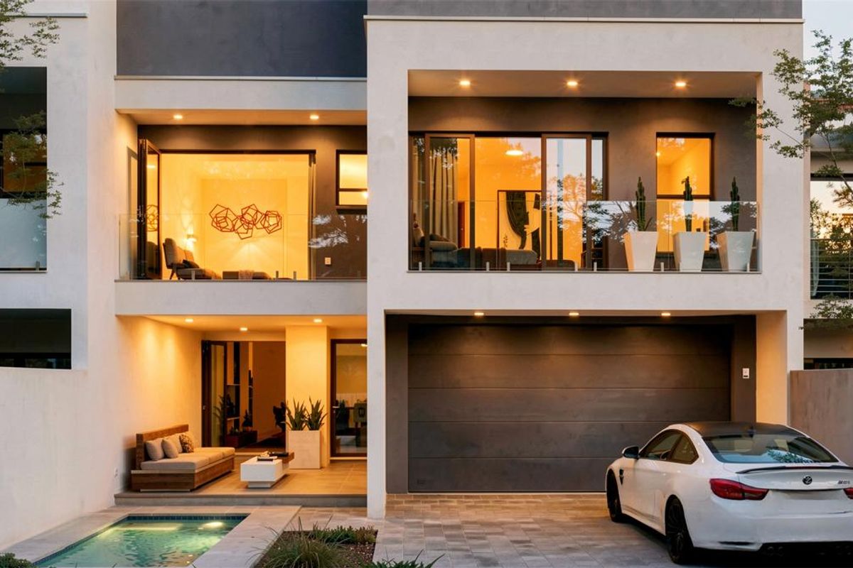 Modern multi-story residence featuring a swimming pool, covered patio, glass balustrades, and an integrated double garage with paved driveway.