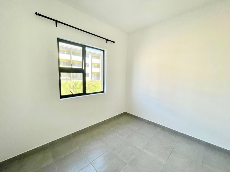 A clean, empty bedroom featuring neutral tiled flooring, white walls, and a modern aluminium window frame with an installed curtain rod.