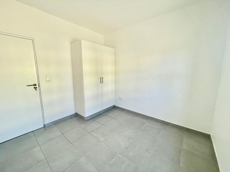 A clean, empty bedroom featuring neutral tiled flooring and a built-in white wardrobe, offering a blank canvas for personalization.