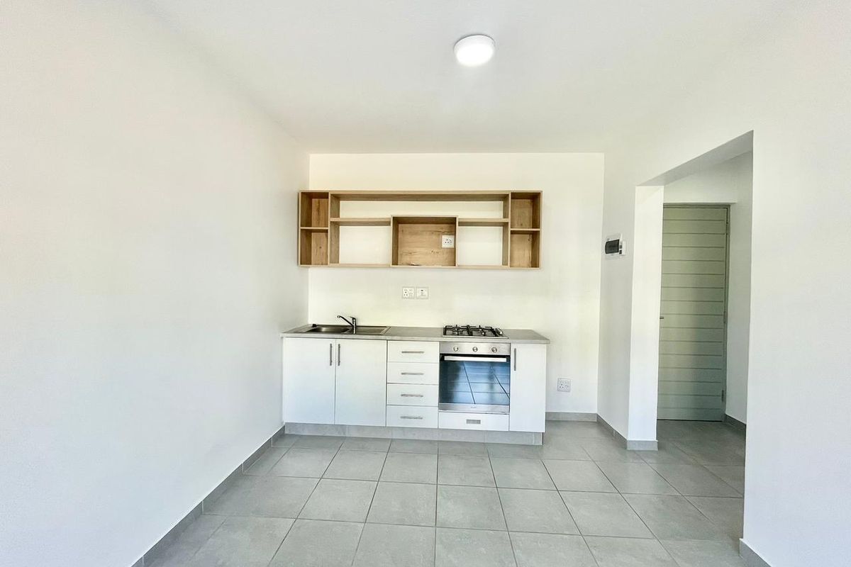 A clean, modern kitchen featuring white cabinetry, built-in oven and gas hob, open shelving, and neutral tiled flooring in an open-plan layout.