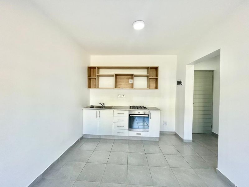 A clean, modern kitchen featuring white cabinetry, built-in oven and gas hob, open shelving, and neutral tiled flooring in an open-plan layout.