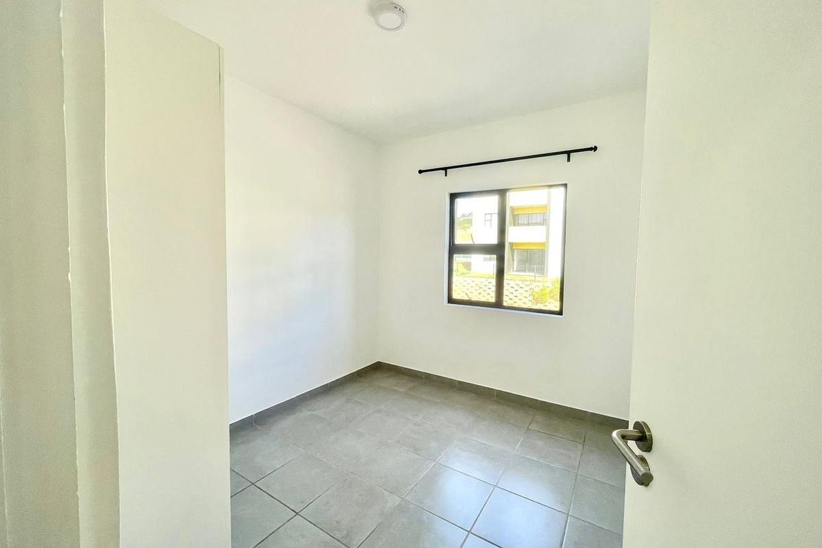 A clean, empty bedroom featuring neutral tiled flooring, white walls, and an aluminium-framed window with a fitted curtain rod.