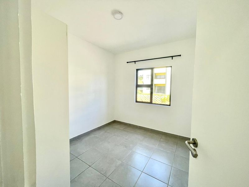 A clean, empty bedroom featuring neutral tiled flooring, white walls, and an aluminium-framed window with a fitted curtain rod.