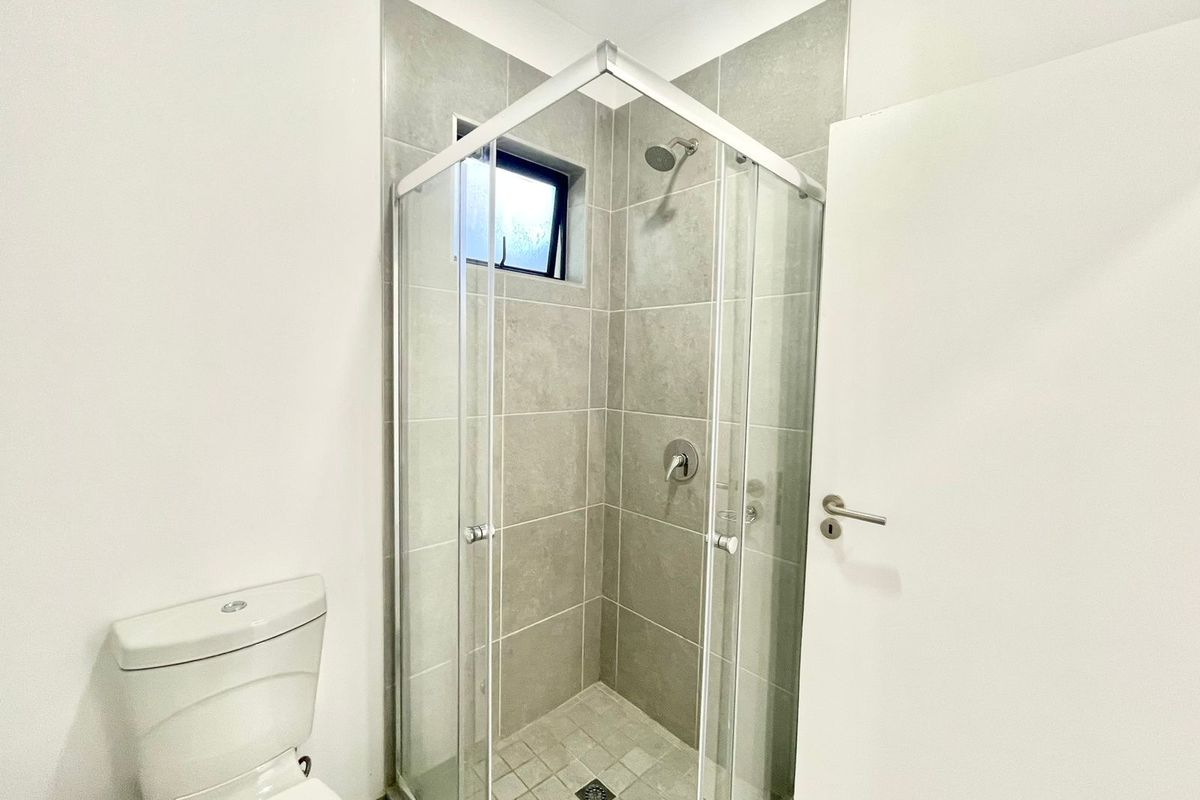 A clean and modern bathroom featuring a glass-enclosed shower with grey tiling and a standard white toilet.