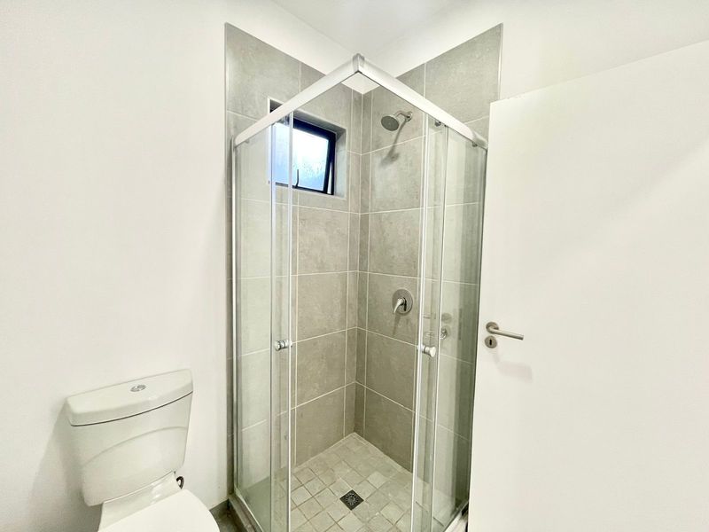 A clean and modern bathroom featuring a glass-enclosed shower with grey tiling and a standard white toilet.