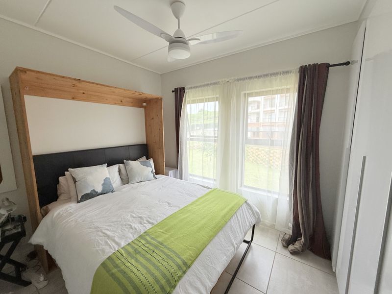 A well-lit bedroom featuring a ceiling fan, tiled flooring, and a built-in wardrobe, offering a comfortable and functional living space.