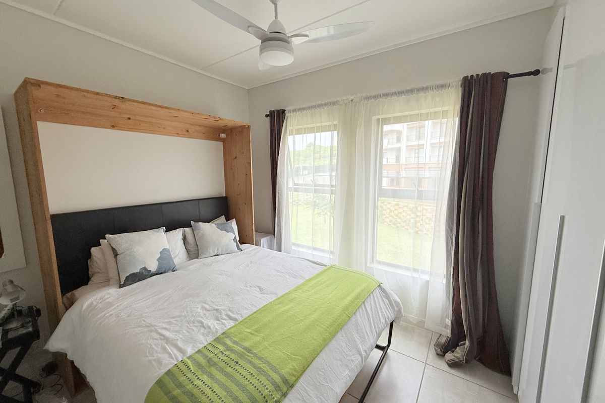 A well-lit bedroom featuring a ceiling fan, tiled flooring, and a built-in wardrobe, offering a comfortable and functional living space.