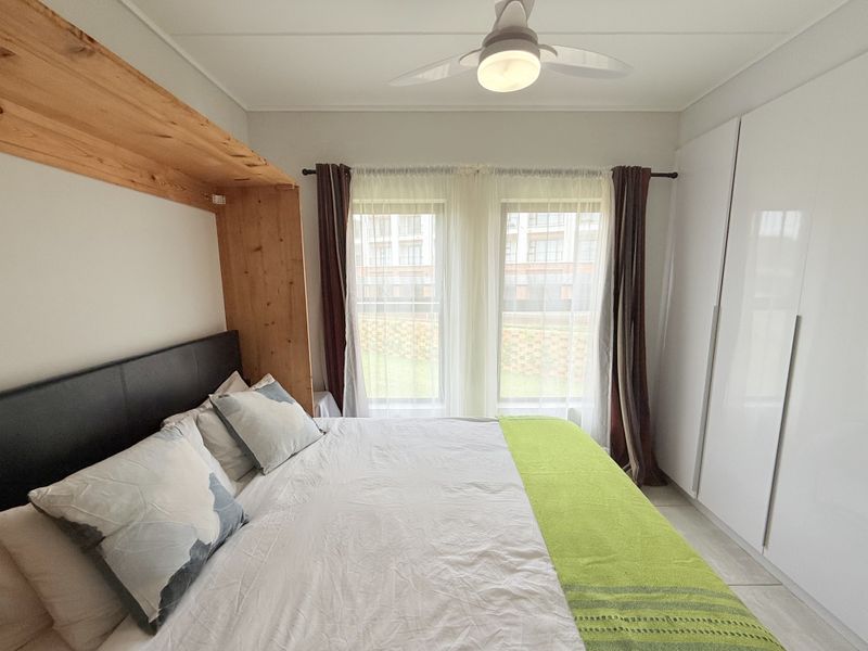 A well-maintained bedroom featuring built-in cupboards, a ceiling fan, and tiled flooring, offering a clean and functional living space.