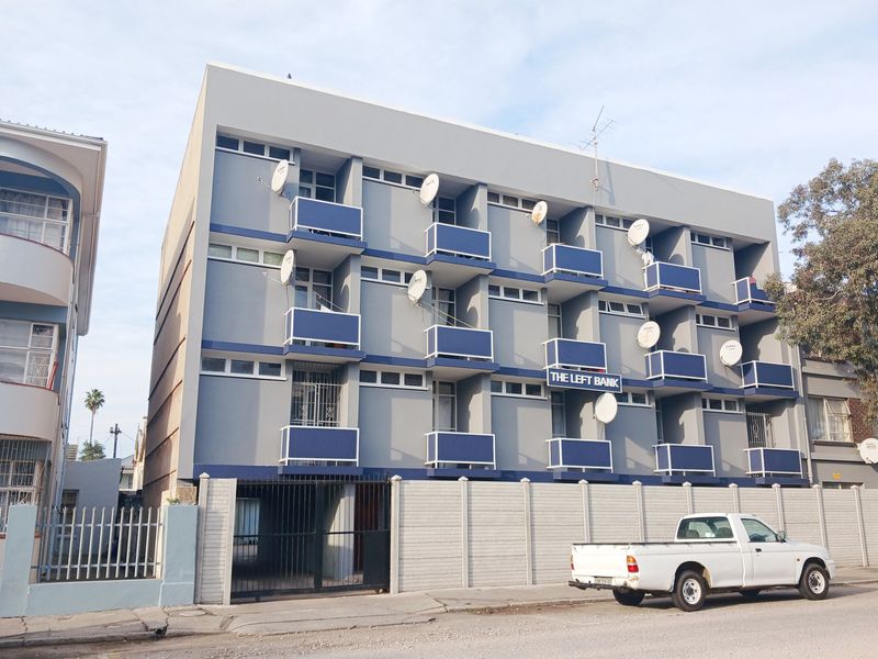 Exterior view of The Left Bank apartment building featuring a multi-story facade with private balconies and a secure gated entrance.
