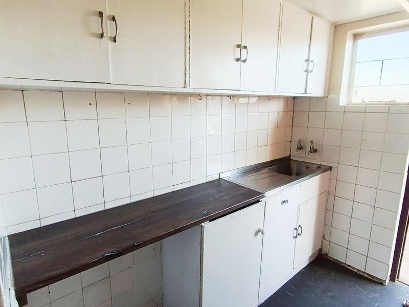 A compact, dated kitchen area featuring built-in white cabinetry, a stainless steel sink, and tiled backsplash, offering potential for a modern renovation.