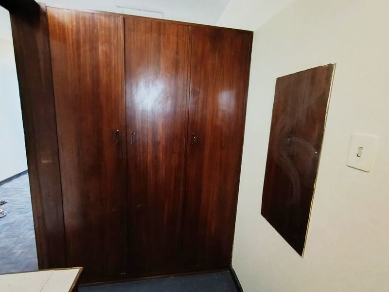 A bedroom interior featuring a large built-in wooden wardrobe and a light switch on the wall.