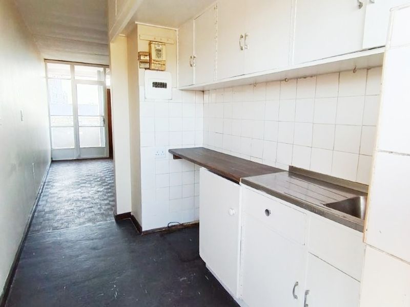 A compact, empty kitchen area featuring built-in white cabinetry, a stainless steel sink, and tiled splashbacks, offering potential for modernization.