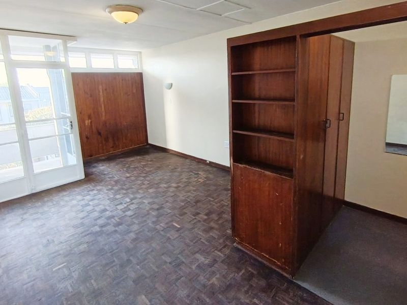 A spacious bedroom featuring original parquet flooring, built-in wooden storage cabinetry, and direct access to an outdoor area through a glass panel door.