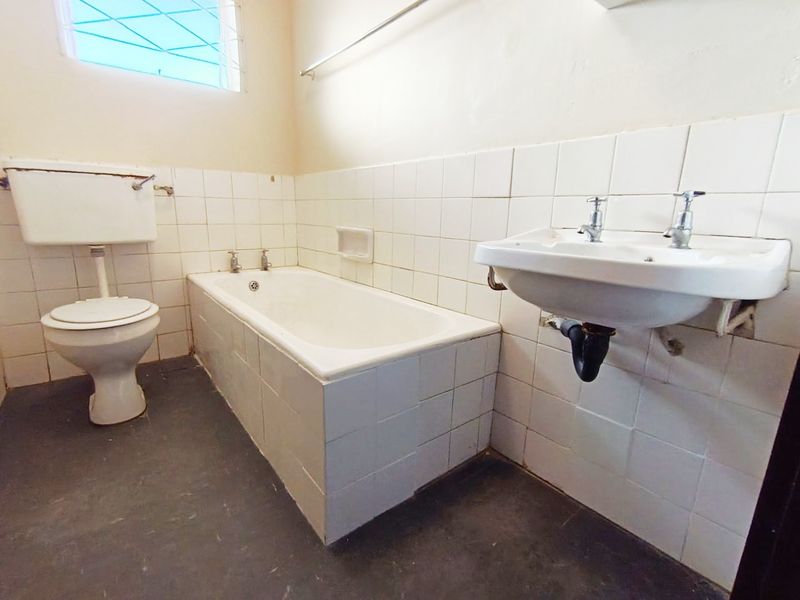 A dated bathroom featuring a standard bathtub, wall-mounted basin, and toilet, requiring modernization of finishes and fixtures.