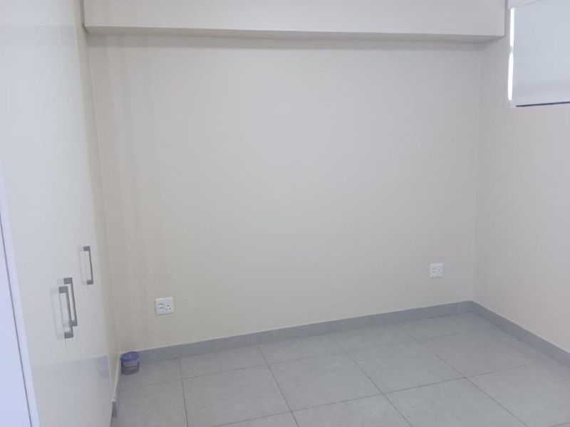 A clean, empty bedroom featuring neutral tiled flooring, built-in cupboards, and a roller blind, providing a blank canvas for personalization.