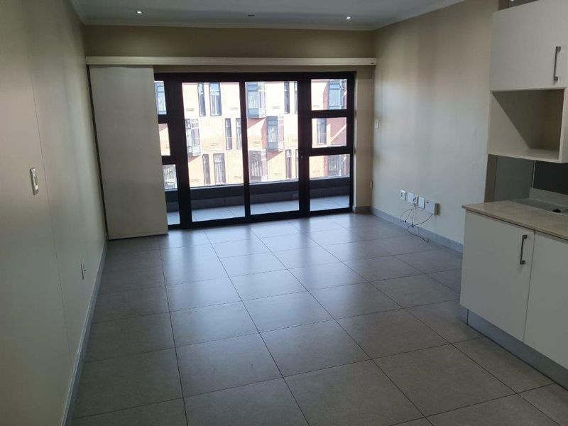 An open-plan living and kitchen area featuring neutral tiled flooring, modern cabinetry, and large sliding glass doors leading to an outdoor balcony.