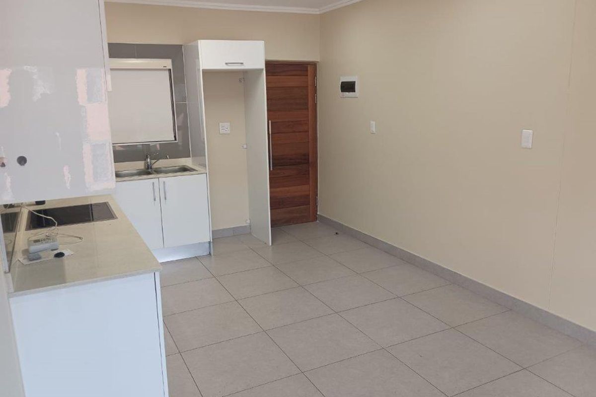 Open plan kitchen and living area featuring tiled floors, modern cabinetry, and a timber entrance door. The space is vacant and ready for customization.