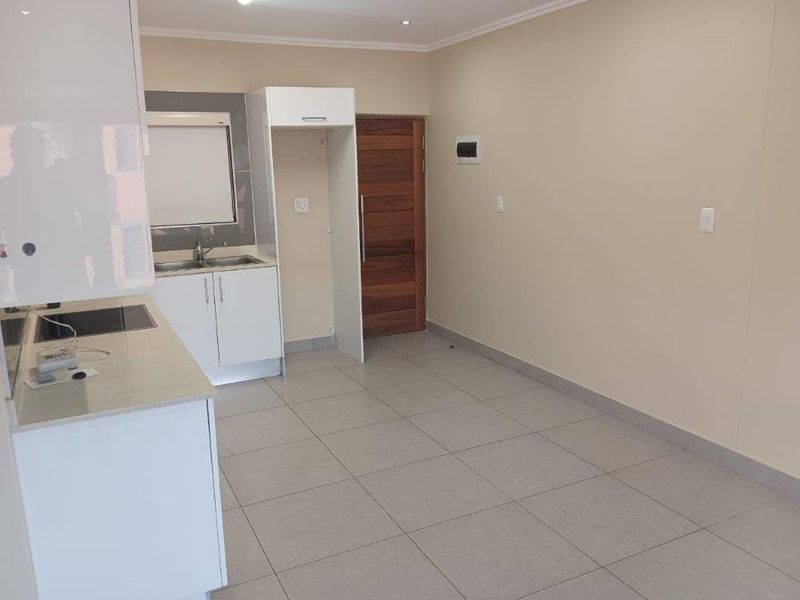 Open plan kitchen and living area featuring tiled floors, modern cabinetry, and a timber entrance door. The space is vacant and ready for customization.