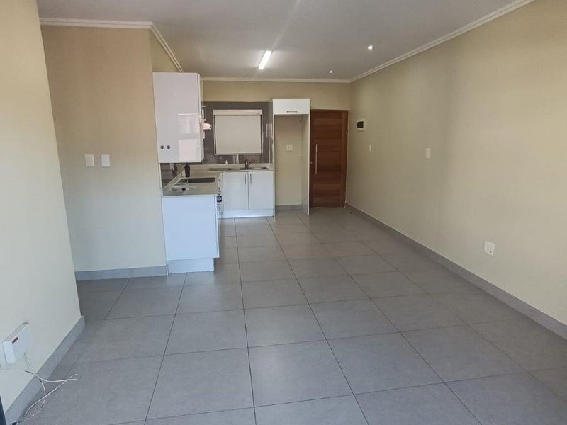 An open-plan living and kitchen area featuring neutral tiled flooring, modern white cabinetry, and recessed lighting in a clean, vacant space.
