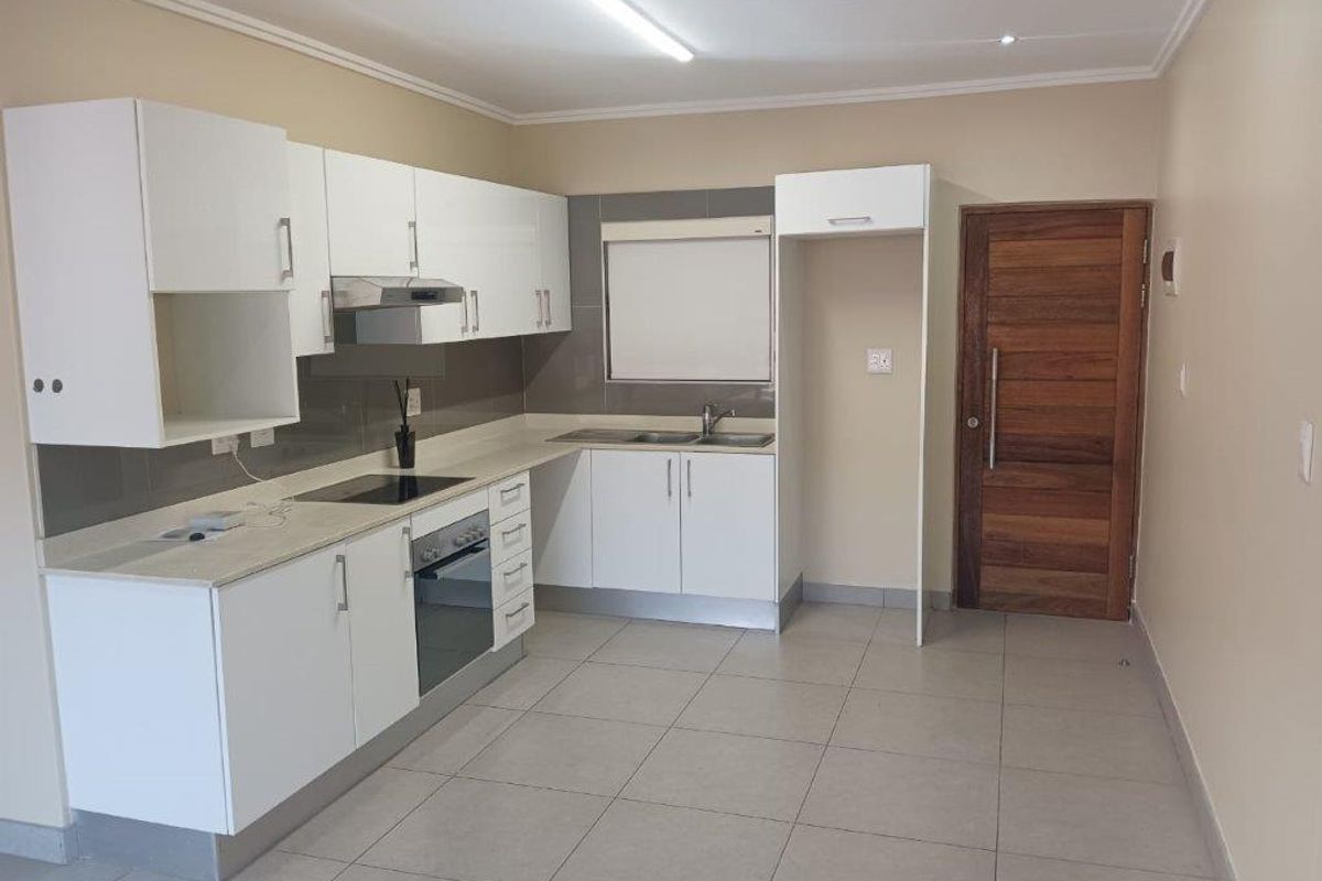 Modern kitchen featuring white cabinetry, integrated electric hob and oven, extractor fan, stainless steel sink, and neutral tiled flooring.