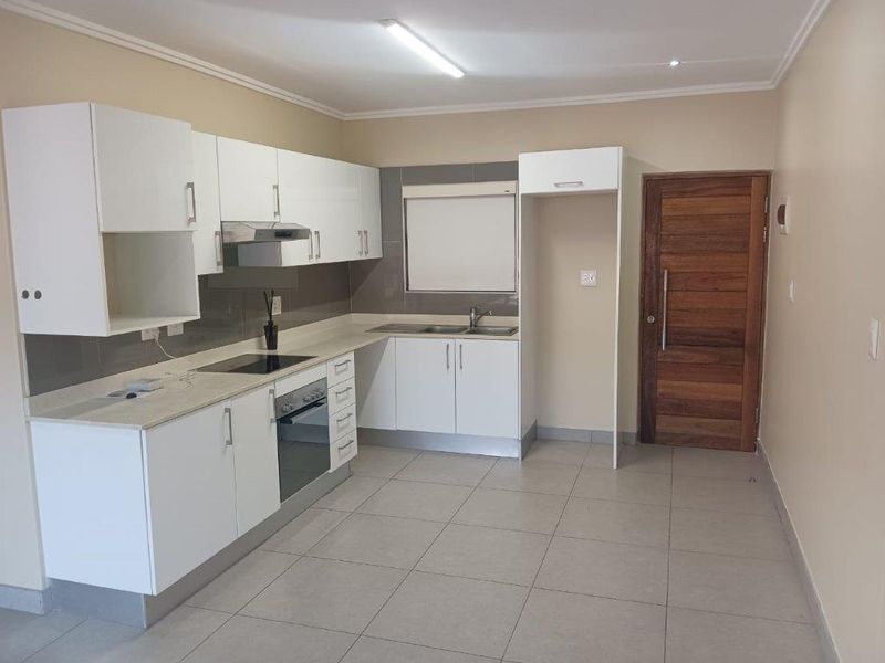 Modern kitchen featuring white cabinetry, integrated electric hob and oven, extractor fan, stainless steel sink, and neutral tiled flooring.