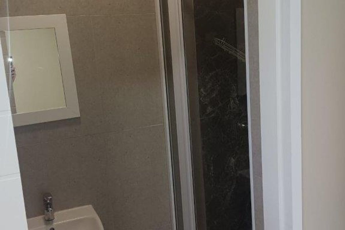 A modern, compact bathroom featuring a wall-mounted basin, tiled walls, and a glass-enclosed shower unit.