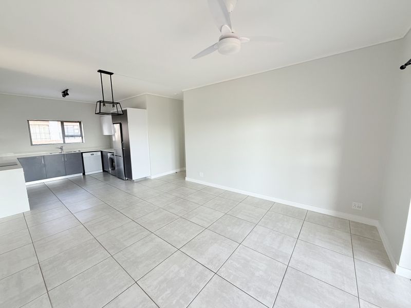 A bright, open-plan living and kitchen area featuring modern grey cabinetry, tiled flooring, and a ceiling fan in a clean, neutral space.