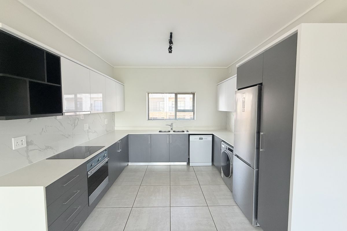 Modern, well-appointed kitchen featuring sleek grey and white cabinetry, stone countertops, marble-look splashback, and integrated appliances in a clean, contemporary layout.