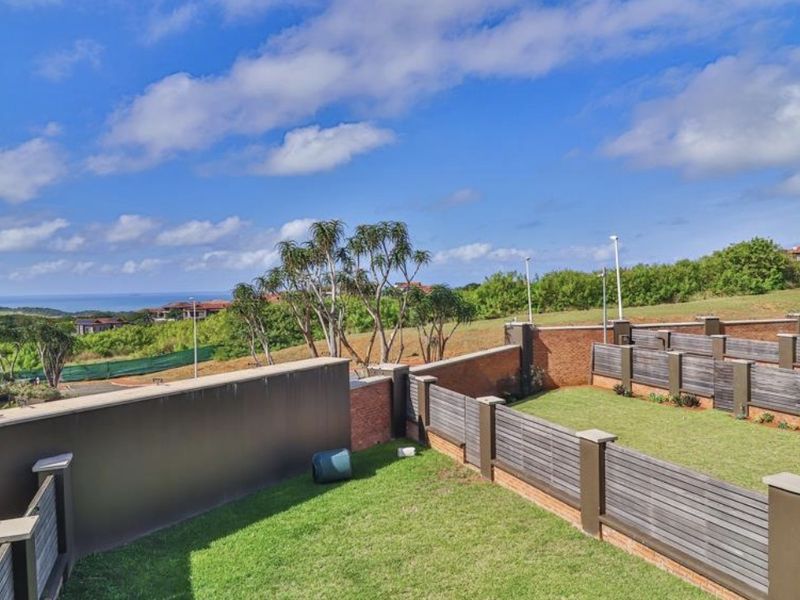 A well-maintained rear garden area featuring brick boundary walls, timber slat fencing, and a manicured lawn with scenic coastal views.