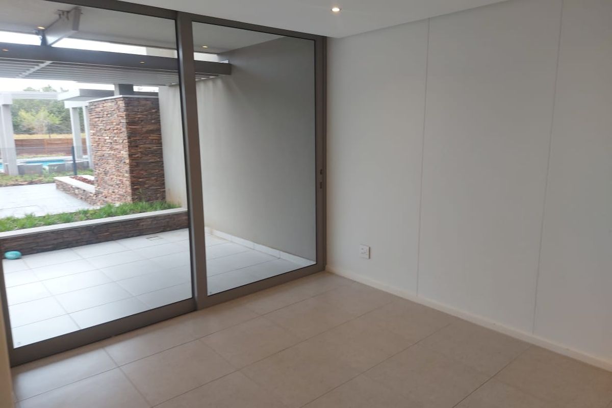 A bright, empty living area featuring large sliding glass doors that open onto a private patio, finished with neutral floor tiles and recessed lighting.