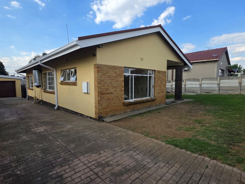 Rear view of the property featuring a paved driveway, detached garage, and a fenced garden area with established boundary walls.
