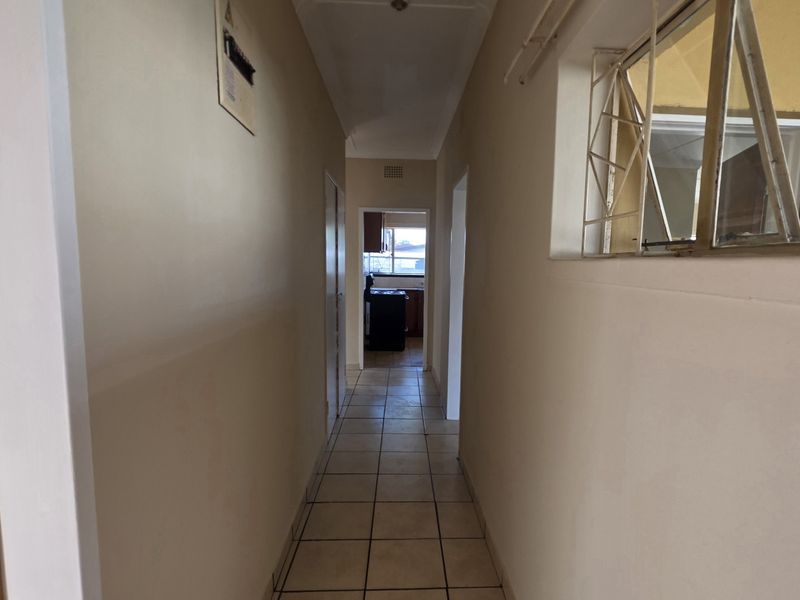 A functional hallway featuring tiled flooring, coved ceilings, and a metal security window grille, providing access to adjacent rooms.