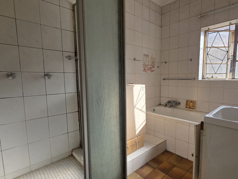 A dated bathroom featuring a separate shower enclosure, bathtub, and pedestal basin with original wall and floor tiling.