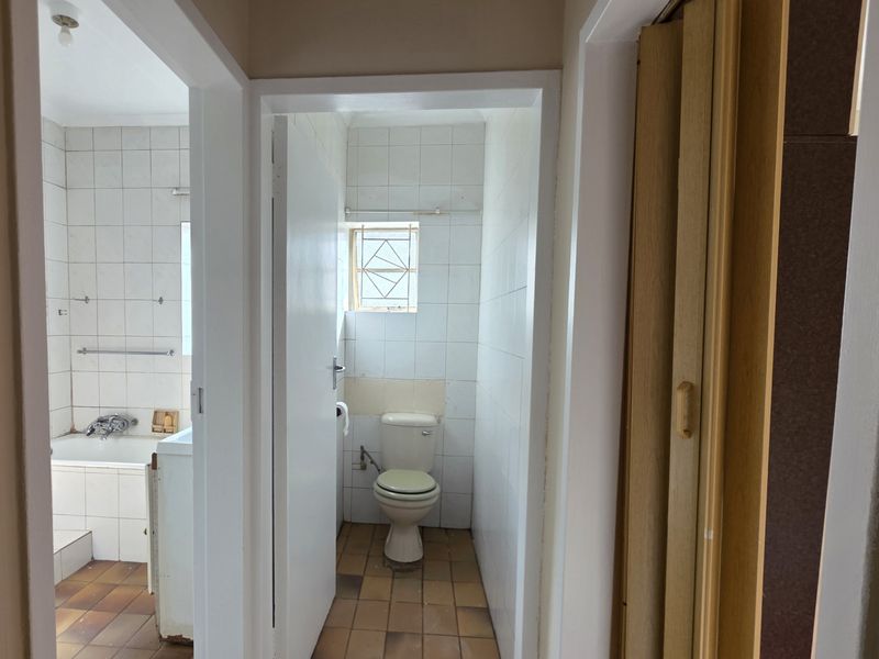 A functional bathroom area featuring a built-in bathtub and separate toilet, with dated tiling and finishes throughout, offering potential for modernization.