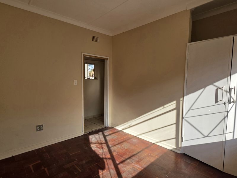 A bright, empty bedroom featuring classic parquet flooring and built-in storage cupboards, offering a clean canvas for personalization.