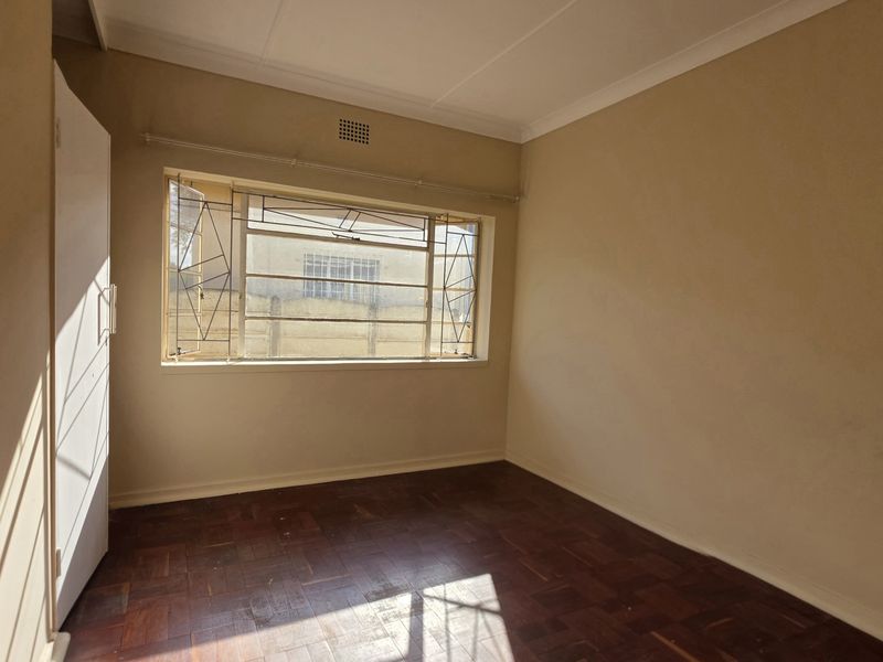 A vacant bedroom featuring original parquet flooring, a built-in cupboard, and security burglar bars on the window.