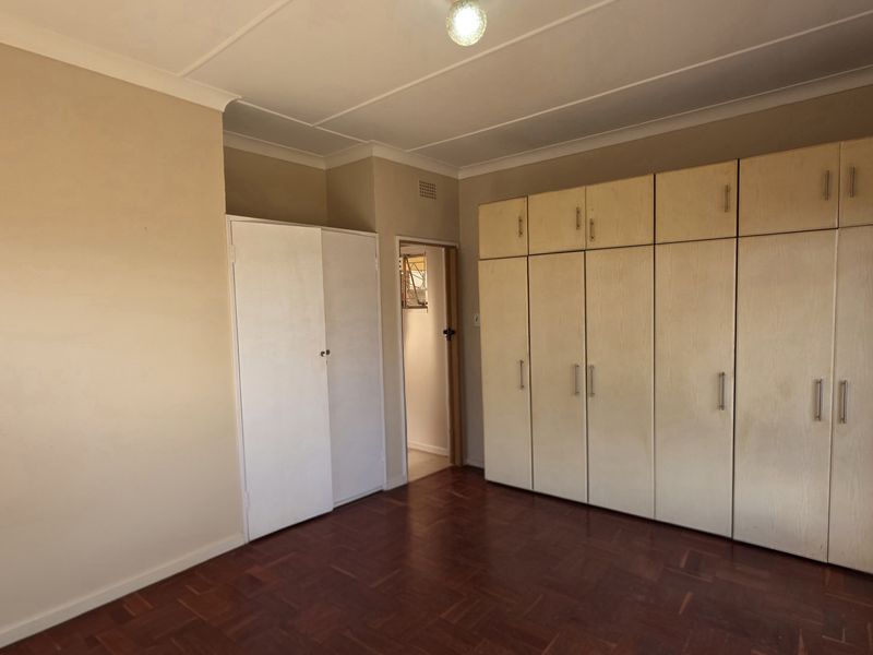 A spacious, empty bedroom featuring classic parquet flooring and extensive built-in cupboard storage, offering a neutral canvas for personalization.