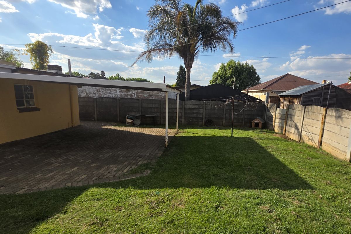 A rear garden featuring a paved, covered patio area and a lawn enclosed by precast concrete boundary walls.