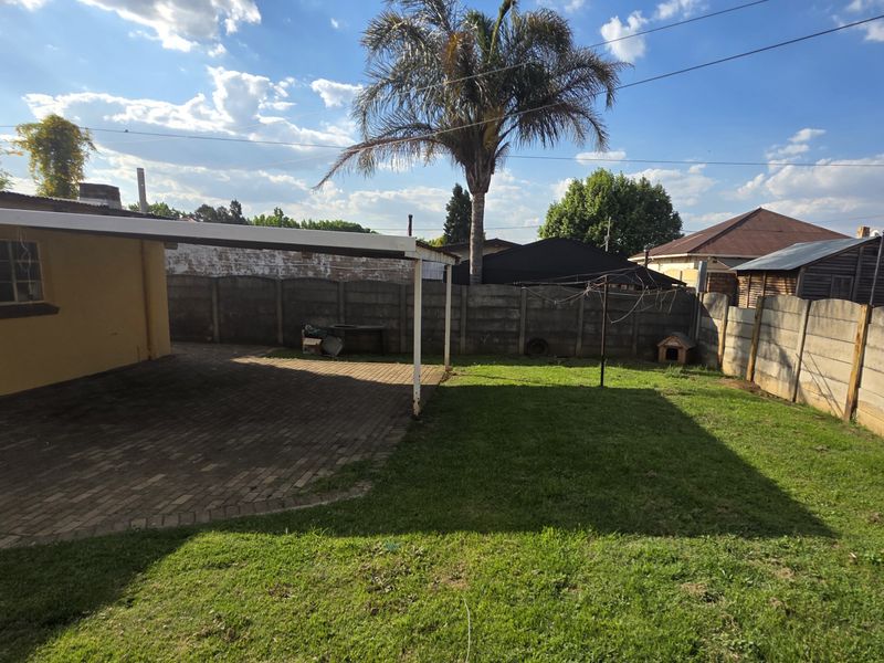 A rear garden featuring a paved, covered patio area and a lawn enclosed by precast concrete boundary walls.