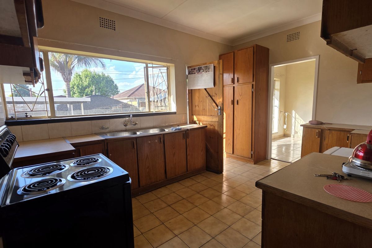 A dated kitchen featuring wooden cabinetry, tiled flooring, and a double sink, offering significant potential for a modern renovation.