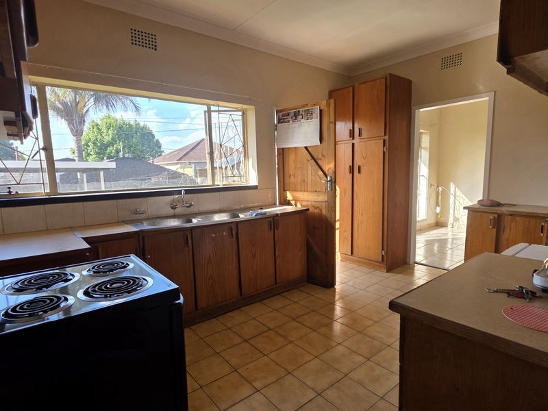 A dated kitchen featuring wooden cabinetry, tiled flooring, and a double sink, offering significant potential for a modern renovation.