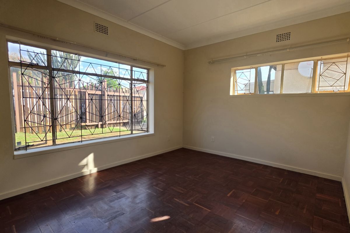 A spacious, empty bedroom featuring original parquet flooring, large windows with security bars, and neutral wall finishes.