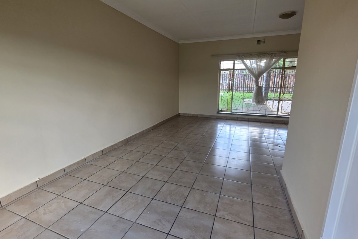 An empty, neutrally painted living room featuring tiled flooring and a large window with security bars, offering a blank canvas for interior design.